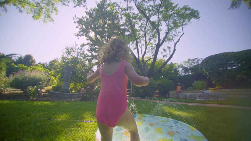 Little girl running in the backyard towards a swimming pool with water jets