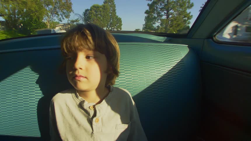 A little boy is sitting inside a car and his face is being illuminated by sunlight