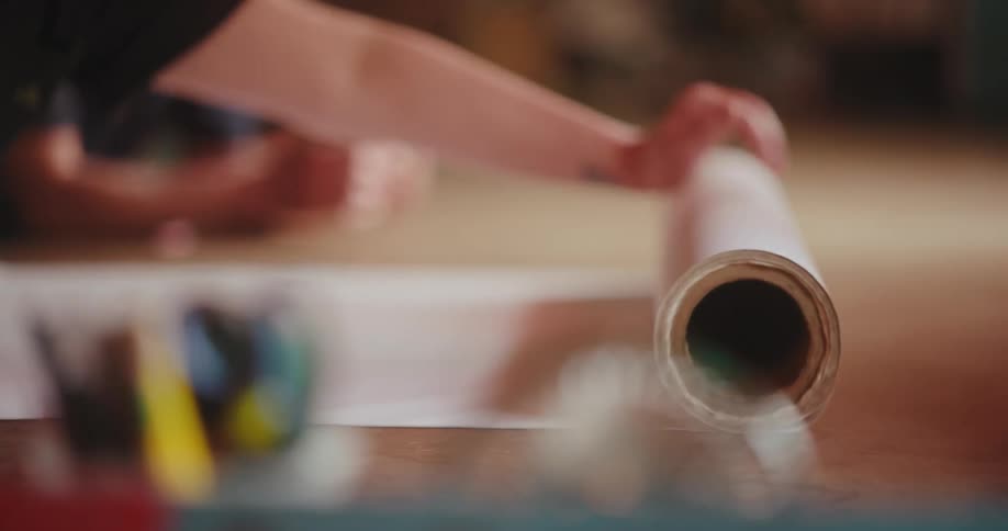 A human hand rolling a white roll of paper on a table