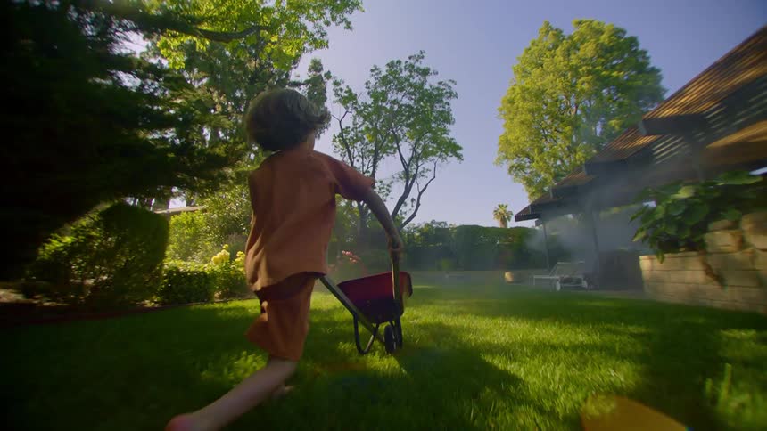 A child pushes a wheelbarrow through the yard