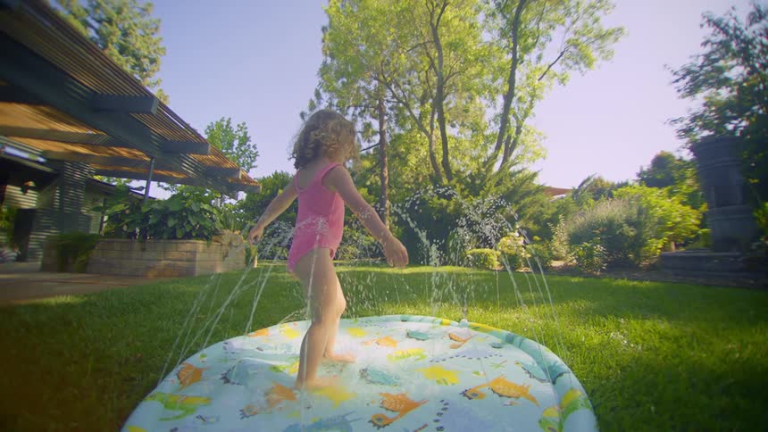 A little girl in a swimsuit is twirling around in a small pool in a grassy backyard