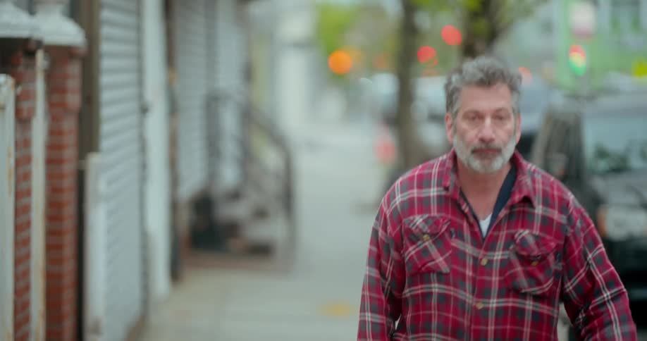A man with gray hair and a red and blue plaid shirt walking on a sidewalk