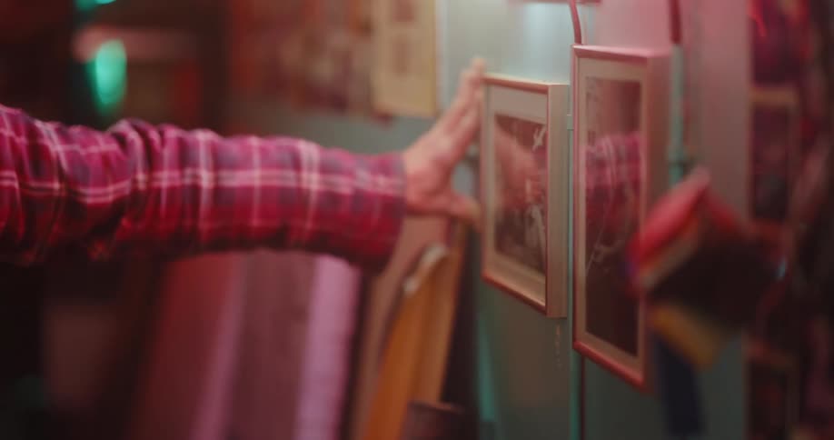 Man indoors crouching to view photos in frames on wall