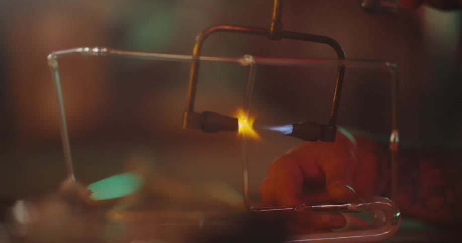 Man with a beard and prescription glasses welding a glass tube with a blowtorch