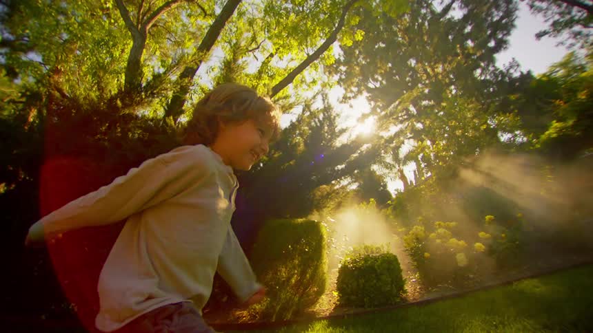 A young boy laughs while running past a garden