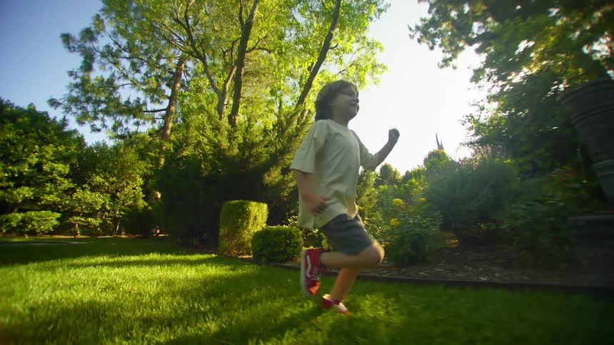 A young boy smiles as he runs through a backyard in slow motion