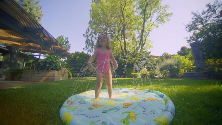 A young girl splashes while standing in a sprinkler pool in her backyard