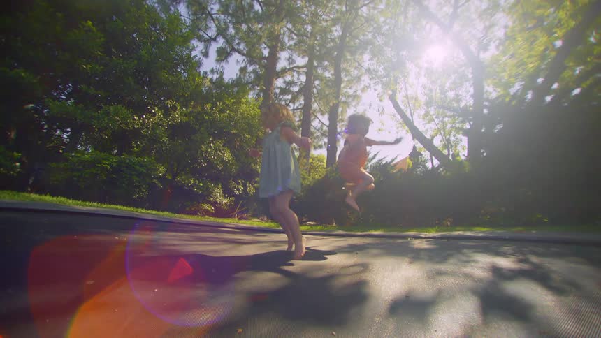 A little boy and a little girl are happily jumping on a large trampoline in a backyard