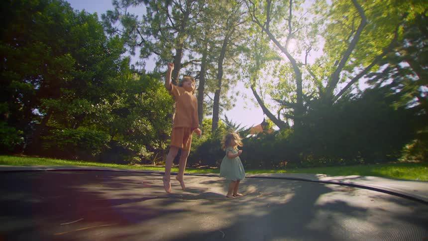 Two small children jumping on trampoline in a garden