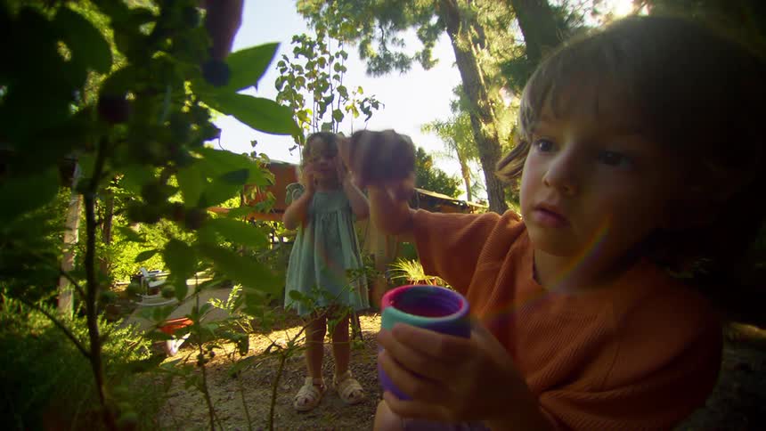 Two young children playing with plants with trees around in a backyard