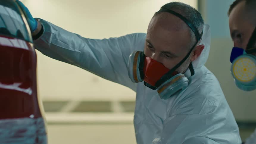 Men with masks and gloves checking the back of a red car with the paint scraped off