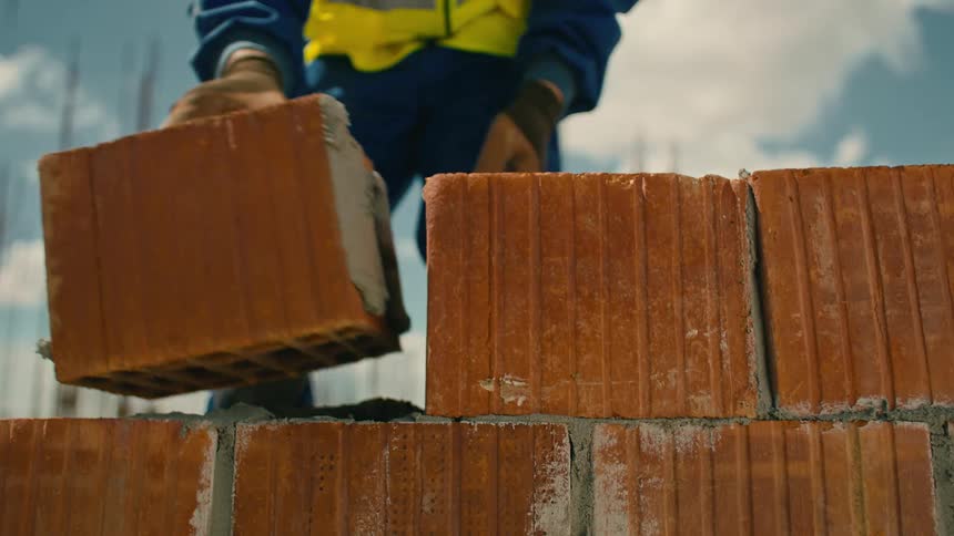 Worker pouring cement and building a brick wall