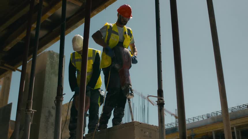 Two construction workers in high visibility vests and hard hats are working on a construction site