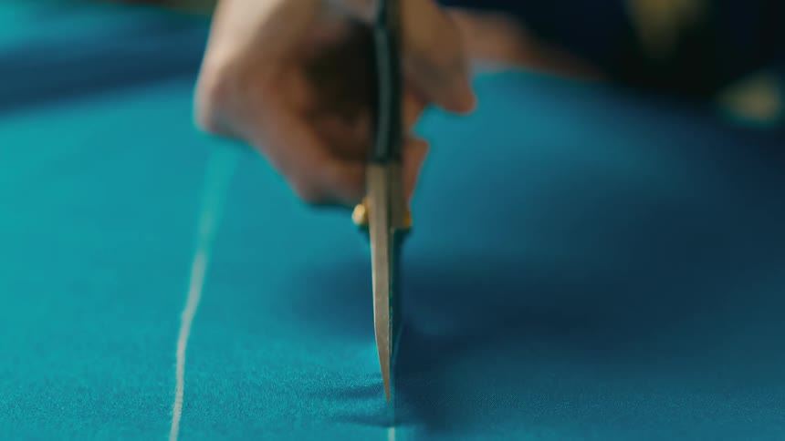 Persons hand cutting straight blue fabric with scissors