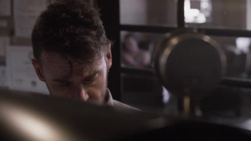 Bearded man in an office looking forward and then looking down towards his desk