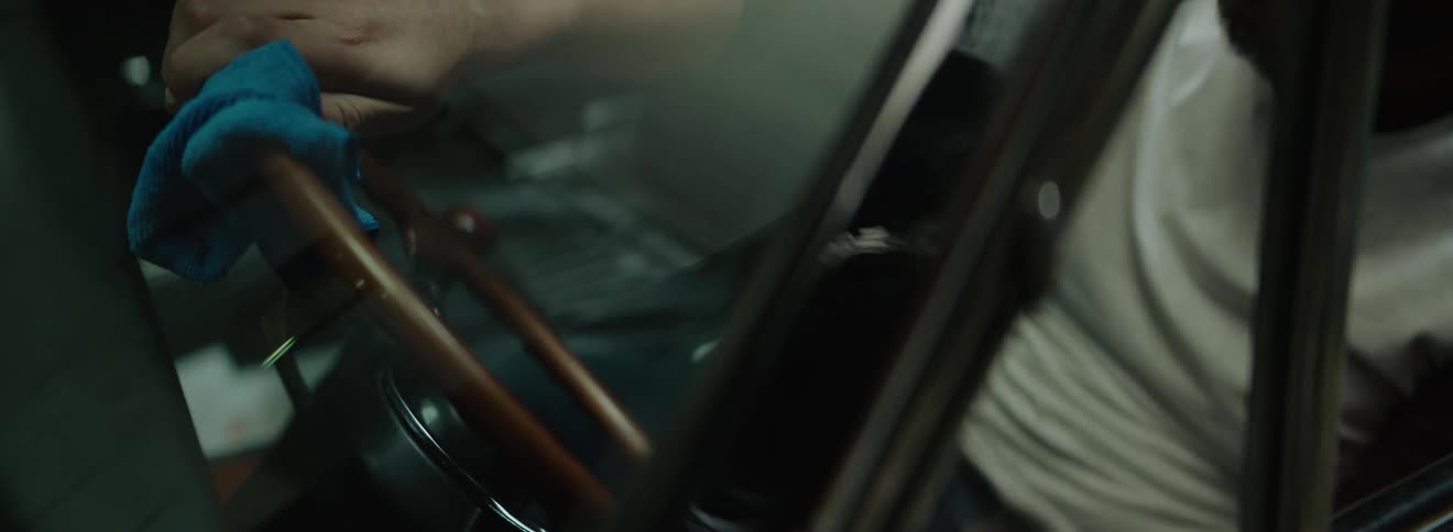 Person sitting in the drivers seat of a car wiping the steering wheel with a blue cloth