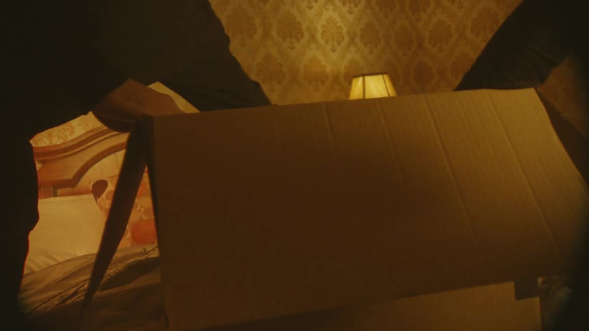 Two people pack a box with bedroom objects on a bed