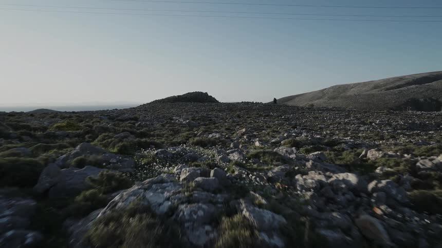 A telephone pole and wires stand in a rocky dry landscape with hills on the horizon