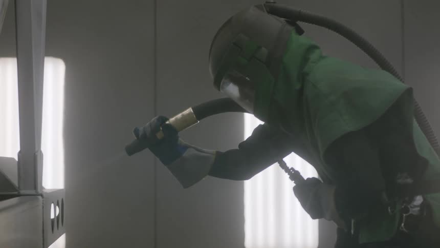 A worker in safety gear sprays down a metal object