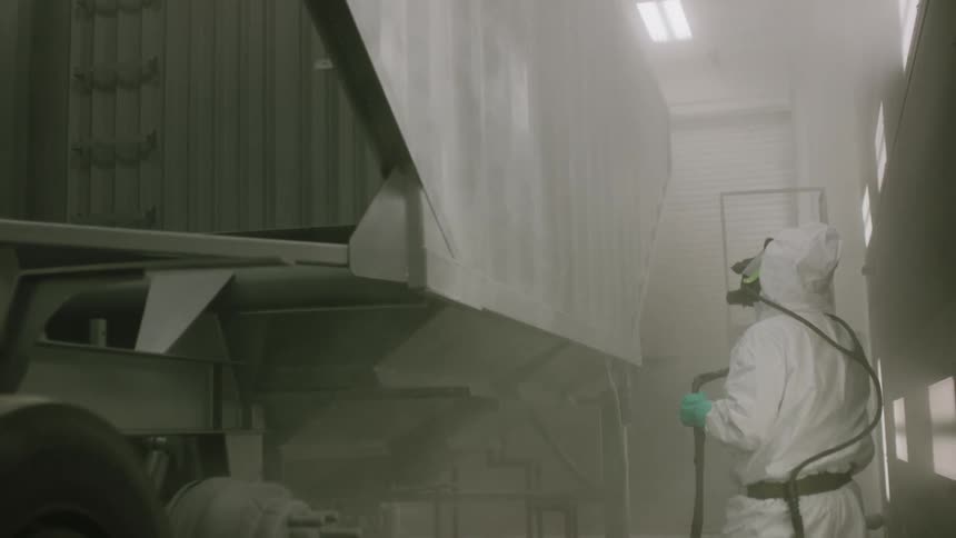 Worker wearing protective gear spray paints panel on a large truck