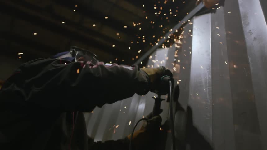 A person in a protective helmet using a grinder on a metal wall and several sparks coming out