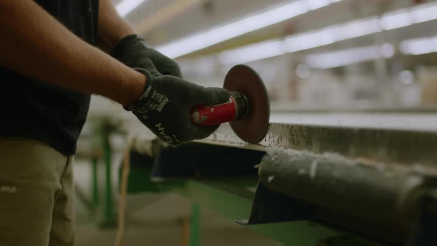 A person wearing black gloves passes a grinder along the corner of a metal surface