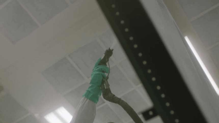 Person wearing a mask and protective clothing using a tool painting an indoor environment