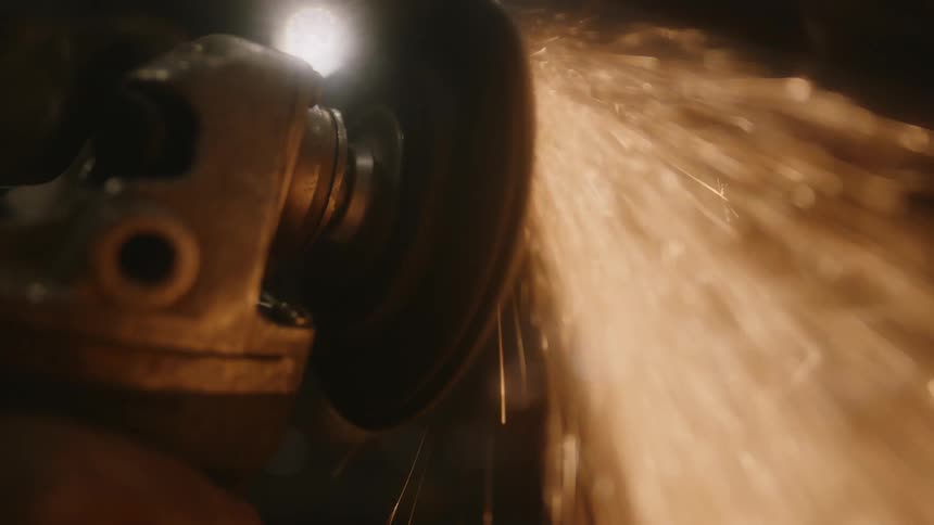 Worker wearing gloves creates sparks while grinding metal with a hand tool