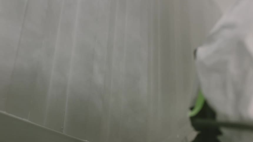 Worker wearing protective gear paints panel white using a spray gun