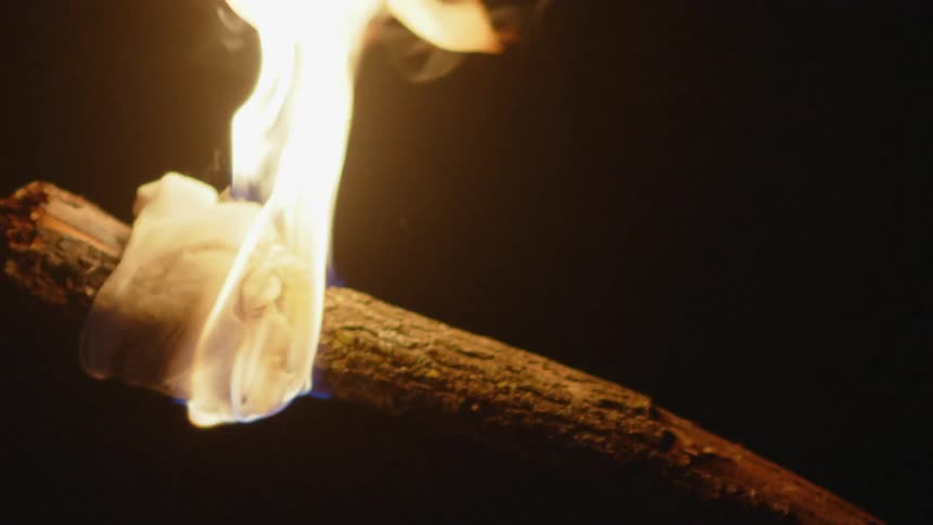 A torch with a piece of white cloth tied to the end and is on fire in a dark environment