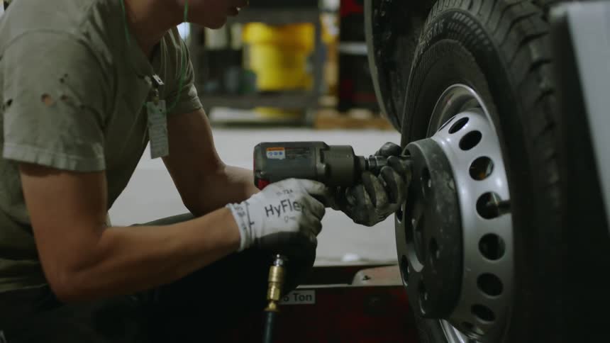 Female mechanic crouching in a garage removes the nuts attaching a tire to a large vehicle