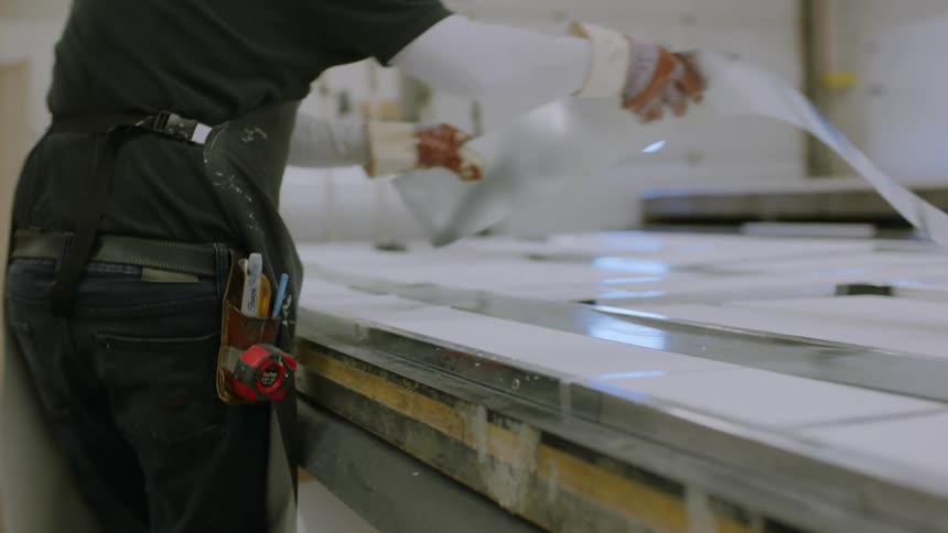 Worker wearing gloves lays metallic strip across other strips lying on a flat surface