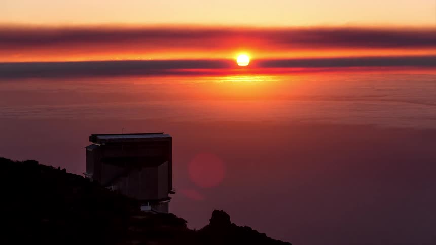 Observatory on a hill in front of the sea of clouds with the sun setting on the horizon