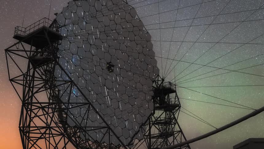 Streaks of light move across a radio telescope as the milky way makes an appearance in the night sky