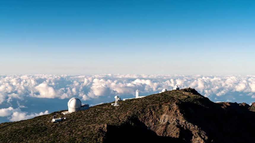 Astronomical observatories on top of a mountain above the clouds under a blue sky