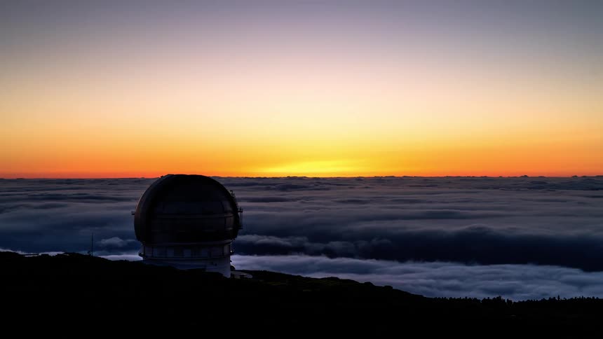 Observatory silhouetted against a vibrant sunset over a sea of clouds below