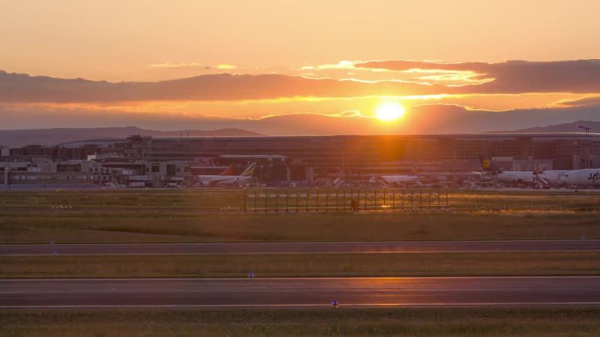 Planes moving with air traffic at an airport with the sun setting on the horizon