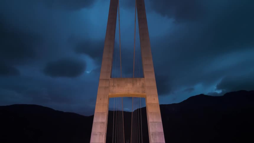 A huge suspension bridge with a street above and clouds passing quickly in the sky
