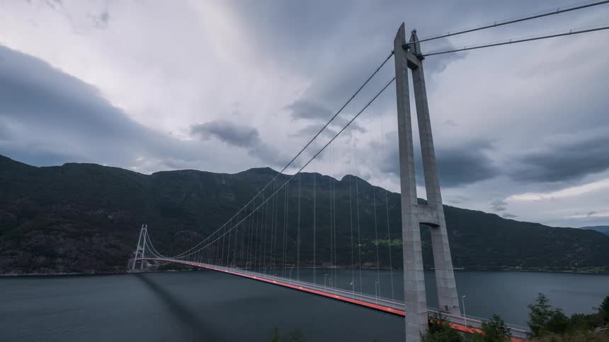 Dark clouds float over a suspension bridge over a river