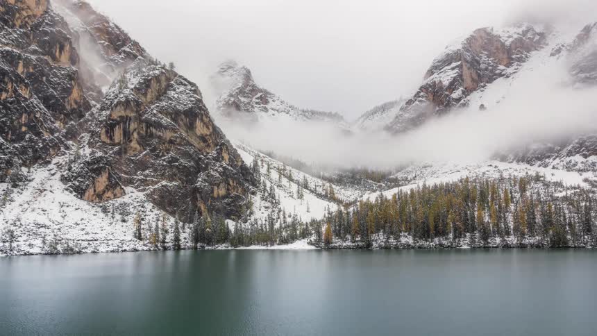 Clouds over a snowy mountain valley near a lake shore