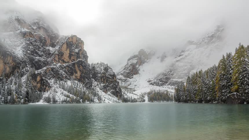 Landscape of a lake surrounded by mountains covered in snow and fog