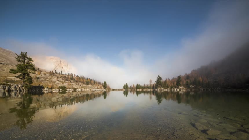 Calm lake surrounded by trees with a gentle mist dissipating