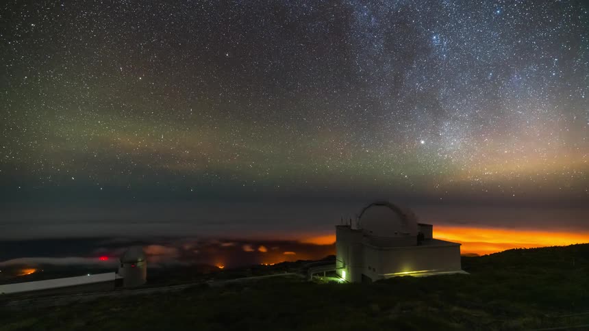 Red tinted low lying clouds and the night sky move past observatory at night