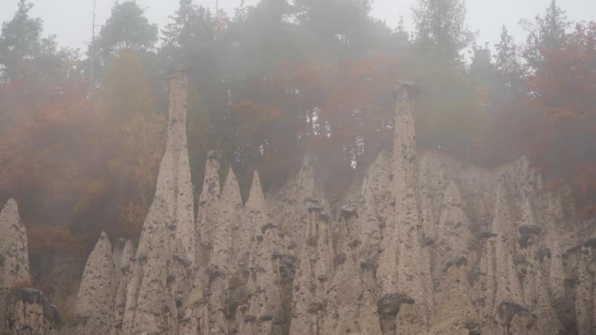 Fog blows by an odd rock formation on the side of a mountain