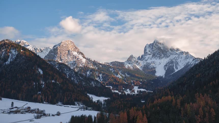Sunlight dims as clouds pass over town surrounded by forested mountains during winter
