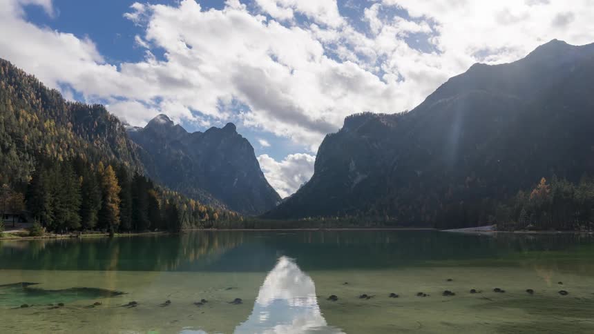 Tranquil lake surrounded by trees and mountains in the background under a partly cloudy sky
