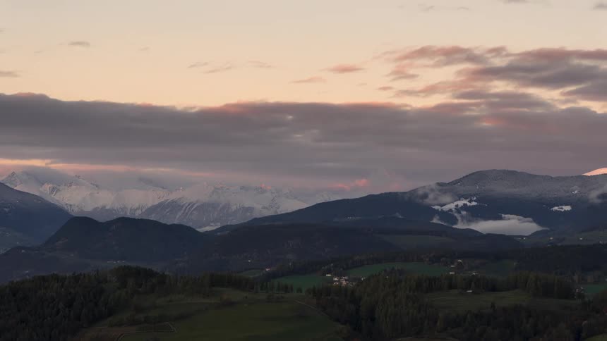 Greenish mountainous landscape with snowcapped peaks against a purple sky