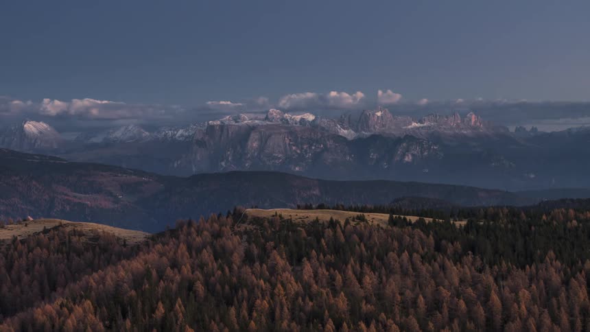 Clouds roll as the sun sets over a forestcovered mountain