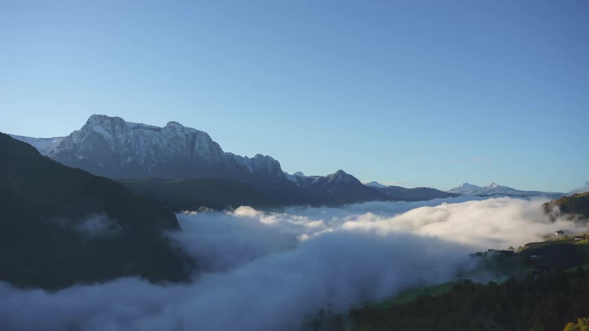 Thick fog covers the base of the mountains under a bright blue sky