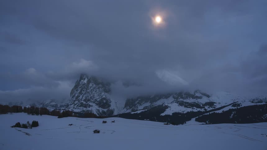 Snowy mountains on a cloudy night with the moon highlighted